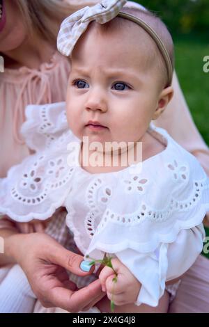 una bambina tiene un fiore tra le mani tra le braccia di sua madre Foto Stock