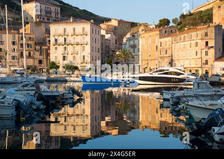 Bonifacio, Corse-du-Sud, Corsica, Francia. Vista sul porto all'alba, edifici lungo la banchina che si riflettono nell'acqua ferma. Foto Stock
