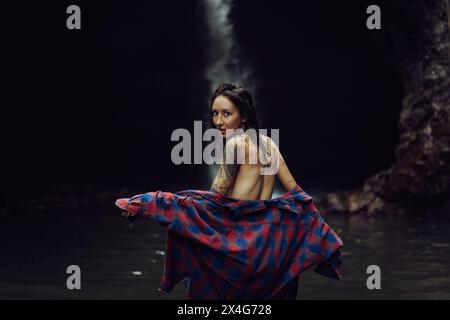 Una giovane donna indossa i vestiti dopo aver nuotato in una cascata. Foto Stock