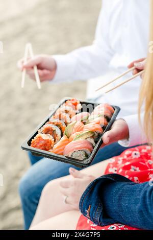Gustate sushi fresco con bacchette in una giornata di spiaggia Foto Stock
