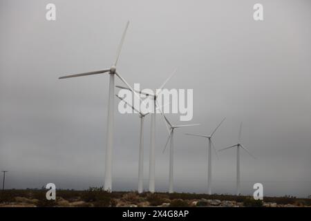 Turbine eoliche che torreggiano su un paesaggio arido e nebbioso. Foto Stock