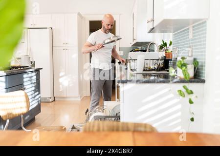 Caricamento dei piatti in una cucina bianca e soleggiata Foto Stock