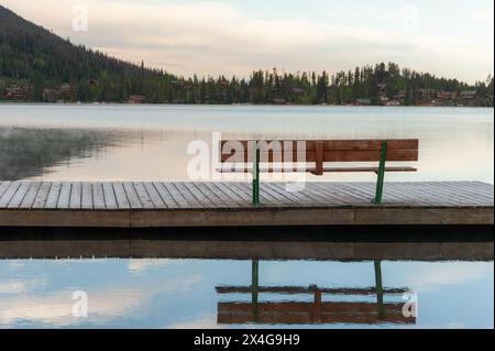 Svuota la panca su un molo nebbioso sul lago all'alba Foto Stock