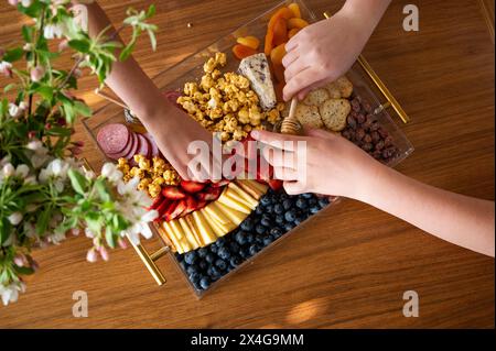Mani che cercano il cibo da un pascolino in una casa luminosa Foto Stock