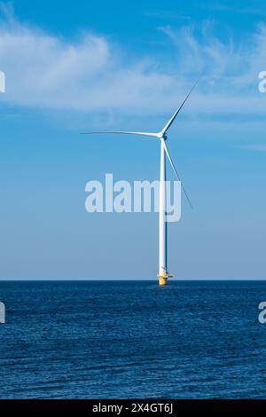 Una turbina eolica solitaria si erge in alto nel vasto oceano, sfruttando la potenza del vento per generare energia pulita per un futuro sostenibile. Turbine a vento in mare, transizione energetica verde in Europa Foto Stock