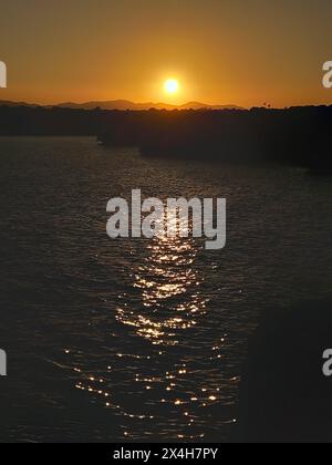 tramonto dell'ora d'oro che proietta una calda luce sul mare calmo, riflettendo la luce dorata sull'acqua con montagne lontane sullo sfondo Foto Stock