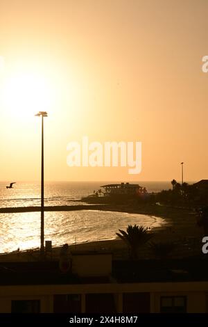 tramonto sulla spiaggia con il sole che tramonta all'orizzonte, proiettando un caldo bagliore sull'acqua e sul paesaggio, catturando la tranquilla fine della giornata Foto Stock