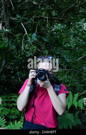 cattura i momenti: giovane donna con fotocamera immersa nella foresta lussureggiante, la luce del sole che filtra tra le foglie creando un ambiente sereno e incantato Foto Stock