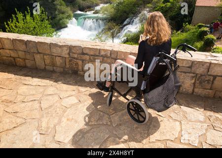 Bambino disabili adolescente turista/ragazza di 14 anni in sedia a rotelle e che gode del Parco Nazionale di Krka da un punto panoramico. Soleggiato giorno d'estate. Croazia. (138) Foto Stock