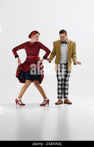 Gioiosa giovane coppia in abiti vintage, uomo e donna che ballano allegramente isolata su sfondo bianco in studio. Posa divertente Foto Stock