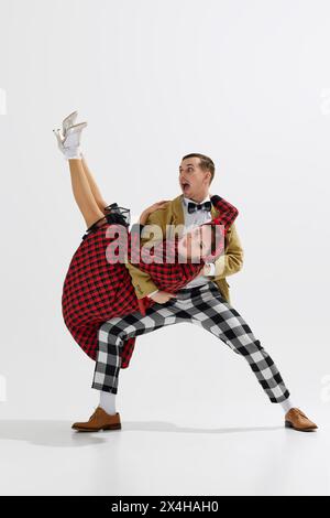 Gioiosa giovane coppia in abiti vintage, uomo e donna che ballano allegramente isolata su sfondo bianco in studio Foto Stock