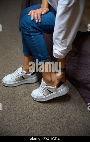 Donna corta che indossa una sneaker seduta sul letto in camera d'albergo di giorno Foto Stock