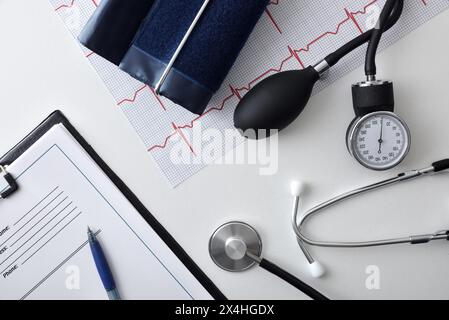 Salute del cuore e controllo della pressione sanguigna con strumenti di misurazione su tavolo medico bianco con cartella ed elettrocardiogramma. Vista dall'alto. Foto Stock