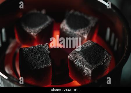 Primo piano di bricchette di carbone incandescenti in un riscaldatore elettrico, utilizzato specificamente per riscaldare i carboni shisha Foto Stock