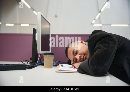 Giovane lavoratore d'ufficio che sta sdraiato sul tavolo e dorme Foto Stock