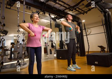Parte inferiore dell'istruttore che insegna a una donna che fa esercizio con i manubri per le spalle Foto Stock