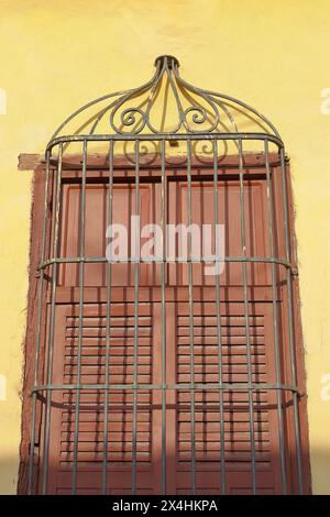 223 il sole del tardo pomeriggio illumina completamente la griglia di una finestra con persiane di legno marroni chiuse, parete gialla di una casa coloniale. Trinidad-Cuba. Foto Stock