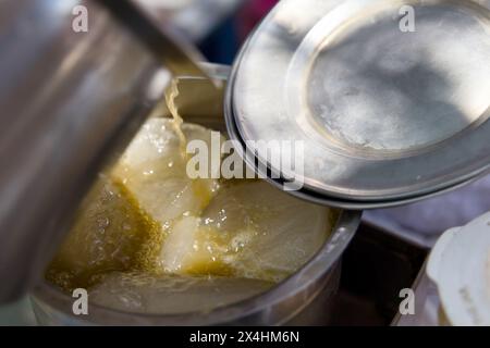 Un venditore versa il succo di canna da zucchero in un bicchiere riempito di cubetti di ghiaccio, creando una bevanda fresca e rinfrescante perfetta per una calda giornata estiva Foto Stock