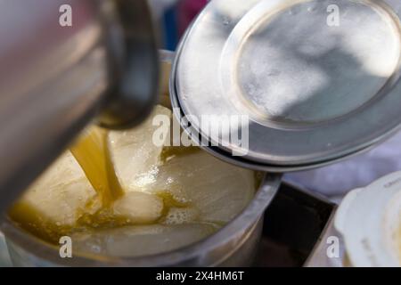 Un venditore versa il succo di canna da zucchero in un bicchiere riempito di cubetti di ghiaccio, creando una bevanda fresca e rinfrescante perfetta per una calda giornata estiva. Foto Stock