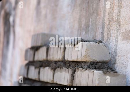 Una pila di blocchi di cemento ben impilata si trova in un cantiere, pronto per essere utilizzato per la fondazione di una nuova casa Foto Stock