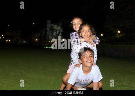 Questa immagine parla di tre bambini felici che giocano insieme nel parco di notte concetto di stile di vita Foto Stock