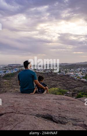 isolare padre e figlio neonato osservando il paesaggio della città in cima alla montagna con un cielo spettacolare al tramonto Foto Stock