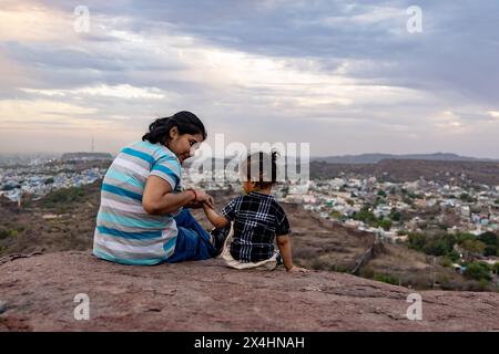 isola madre e figlio neonato guardando il paesaggio della città in cima alla montagna con un cielo spettacolare al crepuscolo immagine è scattata a mehrangarh jodhpur rajasthan india. Foto Stock