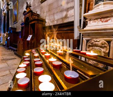 Candele accese in una chiesa con sfondo sfocato che mostra dettagli architettonici. Foto Stock