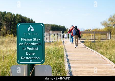 SUPERIOR, WISCONSIN - 5 ottobre 2020: Cartello verde accanto a una passerella sulla duna a Wisconsin Point, con persone che camminano sul passerella di legno. Foto Stock