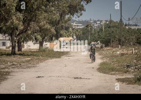 Il povero quartiere di Tunisi, un uomo in bicicletta, la strada polverosa in una calda giornata estiva in Tunisia. Foto Stock