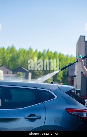 Un uomo lava un'auto nera con una pompa ad alta pressione. Con l'aiuto di una lavatrice portatile. Foto di alta qualità Foto Stock