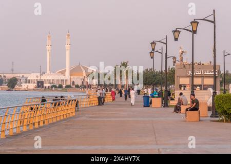 Persone che camminano lungo la Jeddah Corniche (lungomare) in una calda serata estiva in Arabia Saudita. La Moschea di Hassan Enany è vista sullo sfondo. Foto Stock
