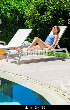 Bella donna che si rilassa vicino alla piscina in un hotel di lusso. Scatto verticale Foto Stock