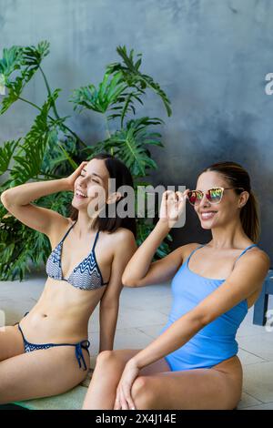 Due donne si godono la compagnia l'una dell'altra mentre siedono a bordo piscina di un lussuoso resort Foto Stock