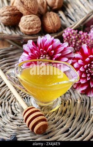 Barca con sugo di vetro e miele, fiori di dahlia sullo sfondo. Cibo sano Foto Stock