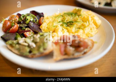 Un nutriente brunch servito con soffici uova strapazzate, una vibrante insalata mista, pane tostato all'avocado e semi Foto Stock
