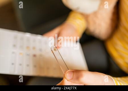 Primo piano di una ragazza che tiene a mano un orecchino preferito su una striscia di plexiglas con un'esposizione di gioielli sfocati sullo sfondo in una gioielleria Foto Stock