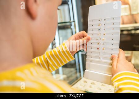 Bambino che esamina vari orecchini su un espositore bianco in una gioielleria Foto Stock