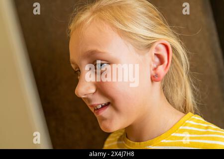 ragazza con un nuovo orecchino, sorridente in una camicia a righe gialle in una gioielleria Foto Stock