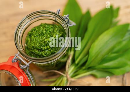 apri il vaso con pesto di aglio selvatico e foglie fresche di aglio selvatico sul legno Foto Stock