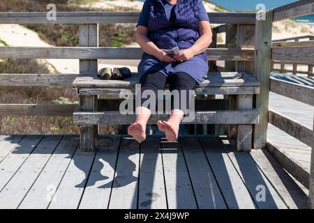 Una donna anziana tiene i piedi bagnati al sole per asciugarsi, causando un'ombra sul ponte sottostante. In attesa che l'acqua evapori. Foto Stock