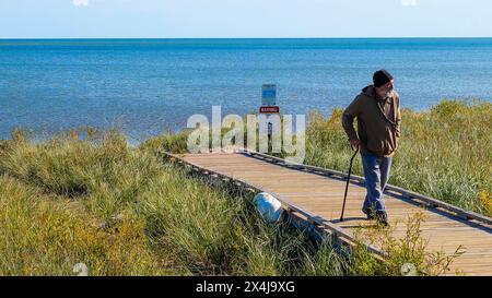 SUPERIOR, WI - 5 ottobre 2020: Un uomo anziano con barba e canna da zucchero passeggia su una passerella sulla riva del Lago superiore in una giornata d'autunno assolata come un cane bianco ex Foto Stock