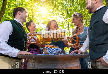 Cameriera che serve birra a un gruppo di persone nel tradizionale tracht all'oktoberfest o birreria all'aperto in germania Foto Stock