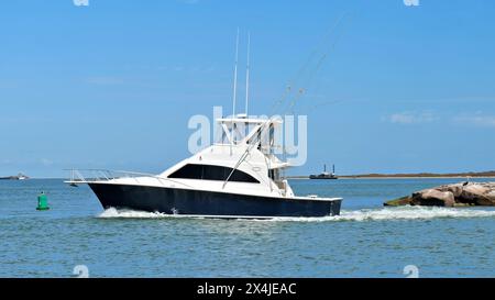 La vista panoramica di uno splendido yacht da pesca bianco e nero naviga oltre la frangiflutti sulle acque blu calme in una giornata di sole. Foto Stock