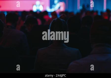 Il pubblico da dietro guarda una presentazione in una sala conferenze buia Foto Stock