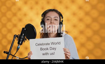 Donna sorridente che filma un video promozionale per la giornata mondiale del libro, isolato sullo sfondo dello studio. Influencer che promuove la lettura, sensibilizzazione per l'evento internazionale globale, camera A Foto Stock