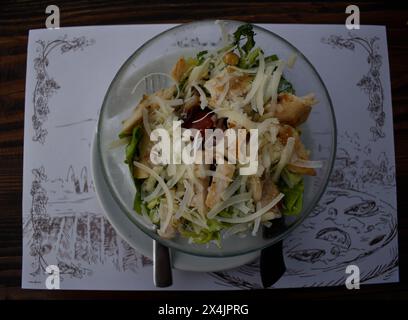 Vista dall'alto dell'insalata Caesar in una ciotola limpida su un tavolo di legno in un ristorante. È costituito da lattuga, crostini, succo di limone, olio d'oliva, uova, formaggio... Foto Stock