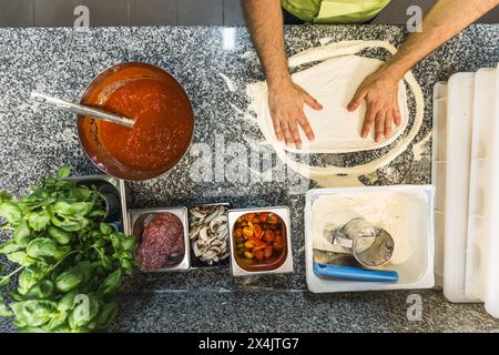 lo chef è circondato da ingredienti che modellano l'impasto per preparare la pizza, vista dall'alto verso il basso. Foto di alta qualità Foto Stock