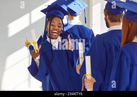 Black Female Graduate celebra il successo con Diploma e Thumbs Up Foto Stock