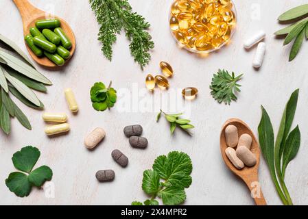 Le vitamine naturali, gli integratori vegetali e le foglie verdi piatte si trovano su fondo di legno bianco. Varie capsule e pillole organiche. Foto Stock